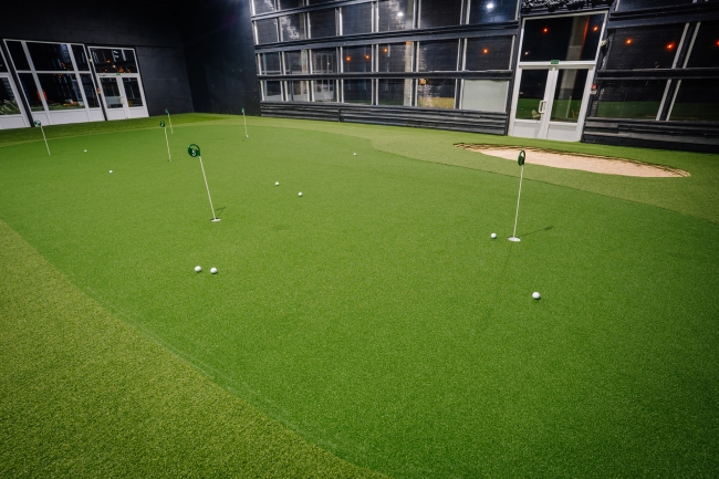 Golfa ripināšanas grīns telpās ar vairākām bedrītēm un karodziņiem